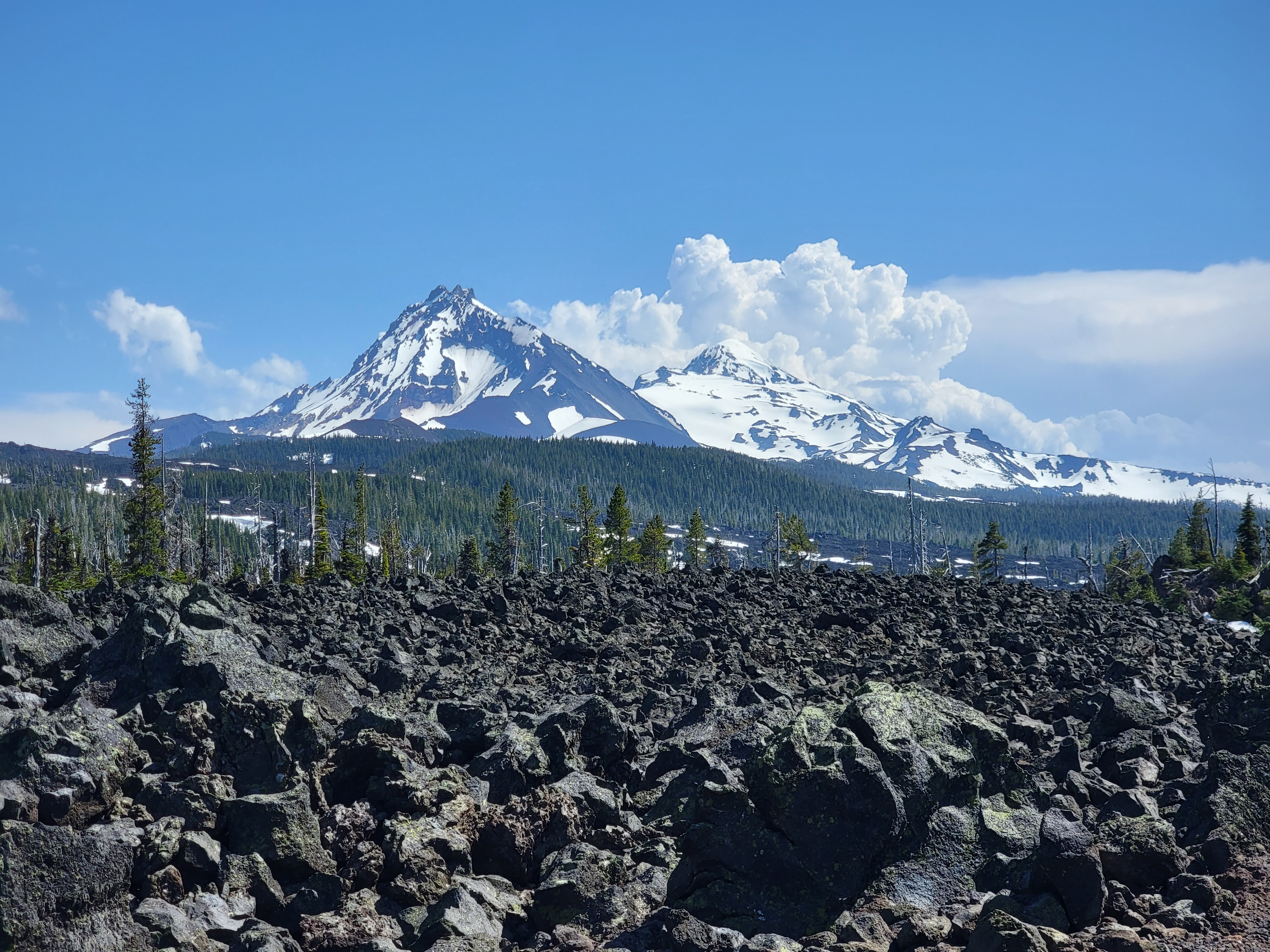 A picture of lavarock and mountains, with a blue sky in the background, taken from the top of the McKenzie Pass